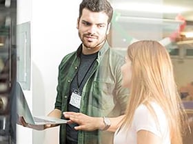 Man holding laptop and explaining something to his teammate